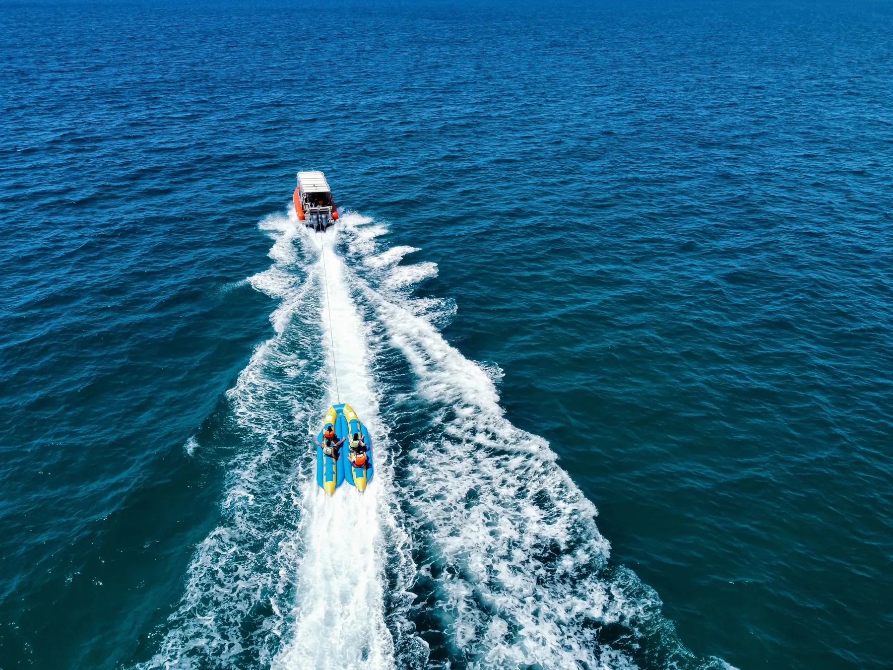 A group of riders holding on during a banana boat ride across blue water