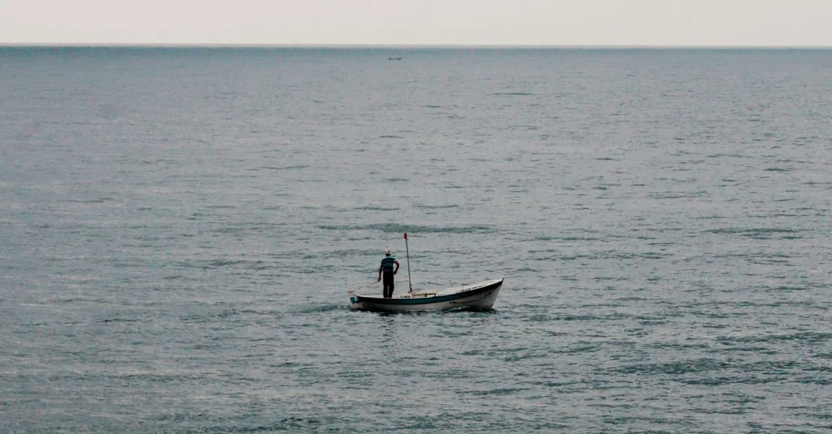 An angler fishing from a small open boat on calm blue water