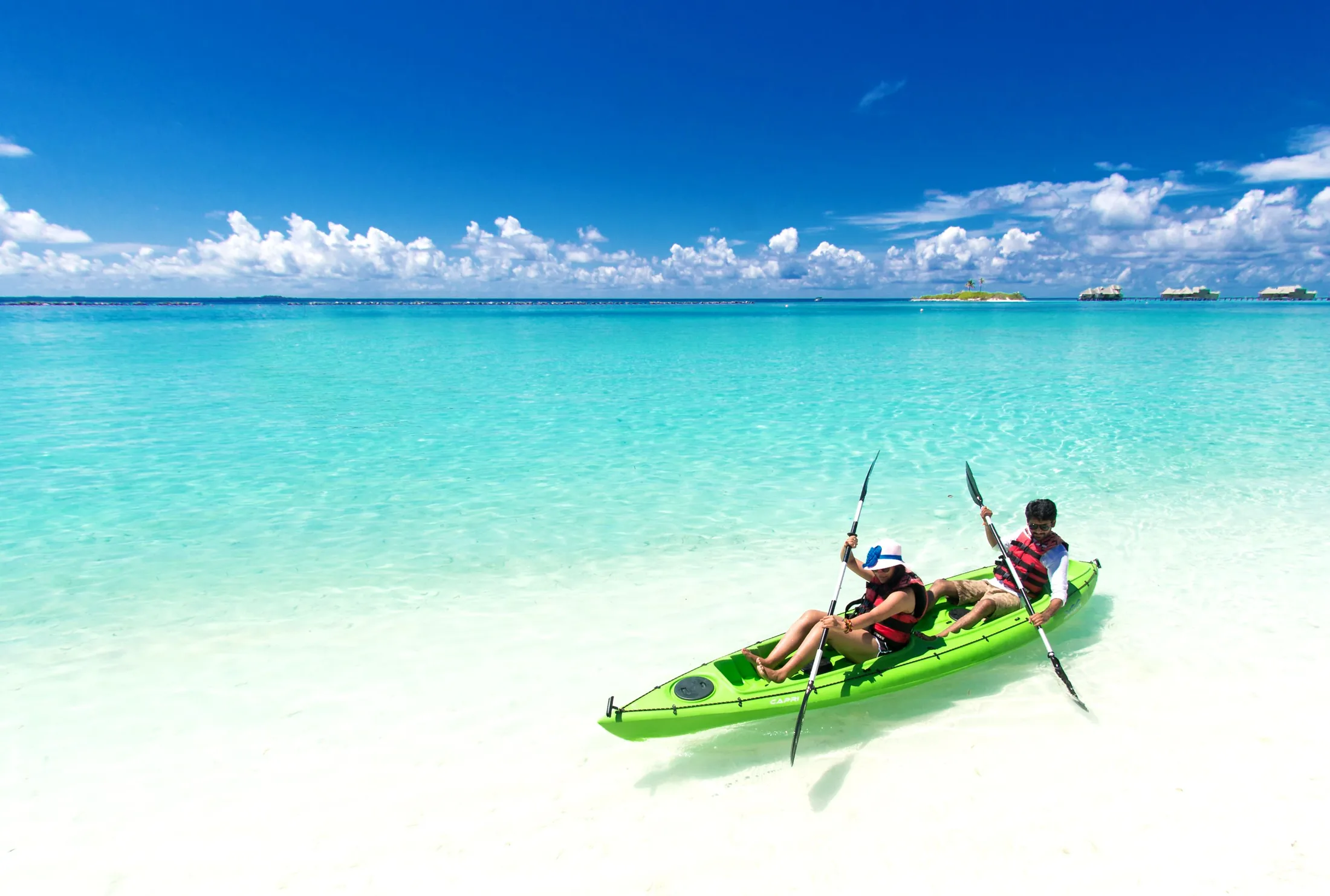 Two people paddling a sit-on-top kayak across calm blue water